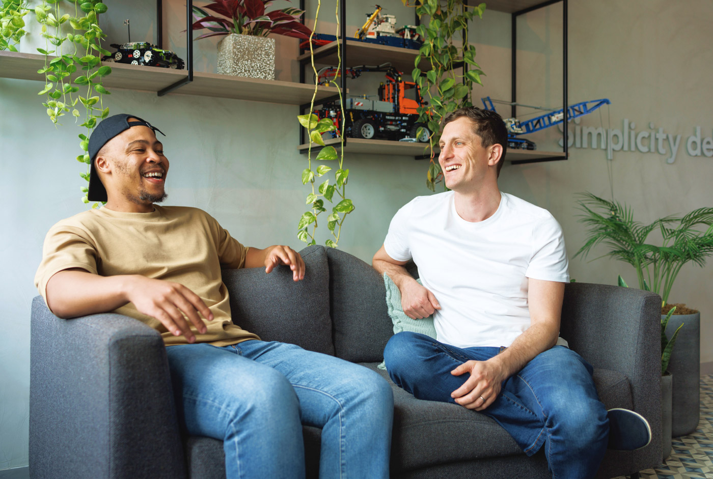 Two guys sitting having a conversation on a grey couch